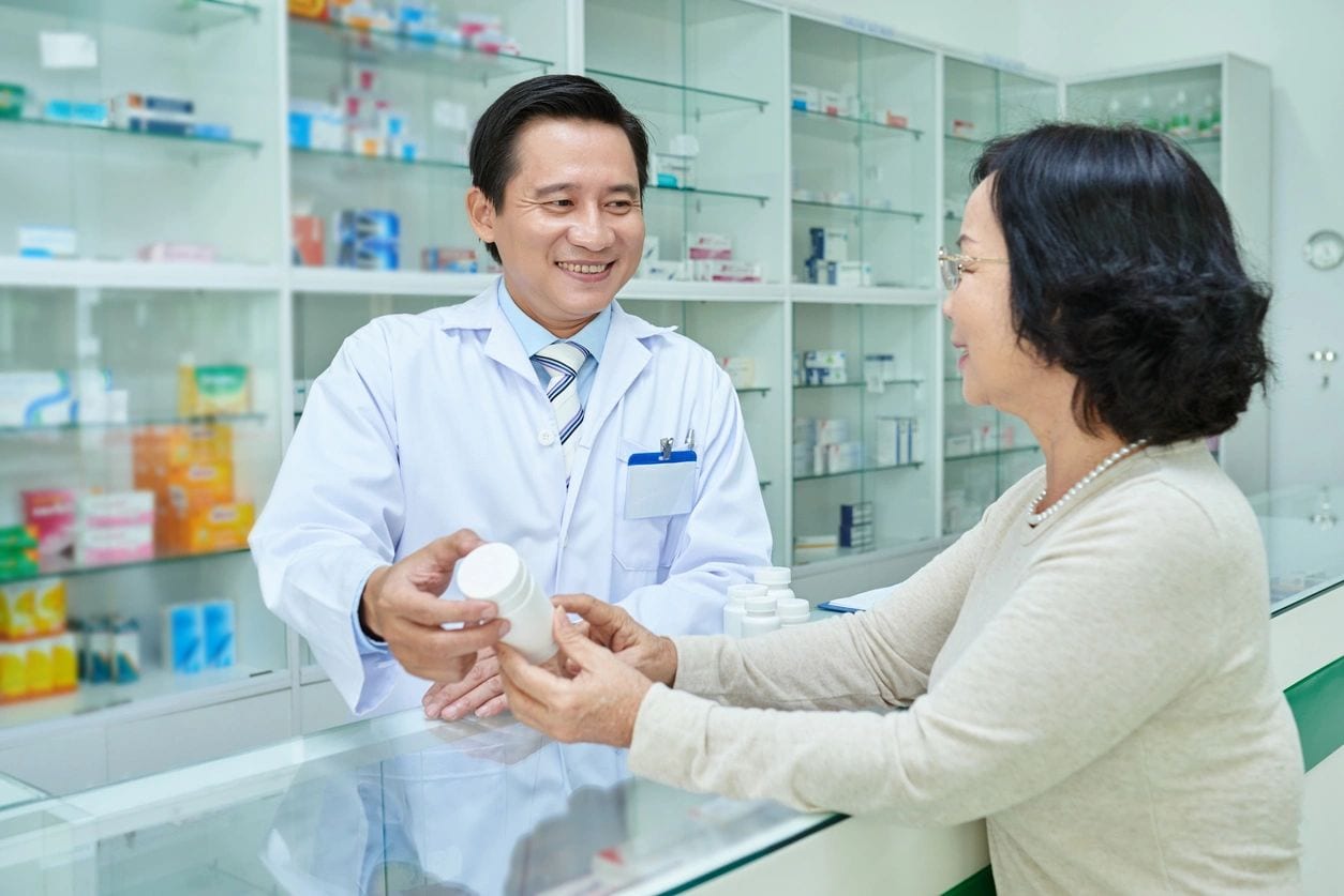 A woman is handing a bottle to a pharmacist.